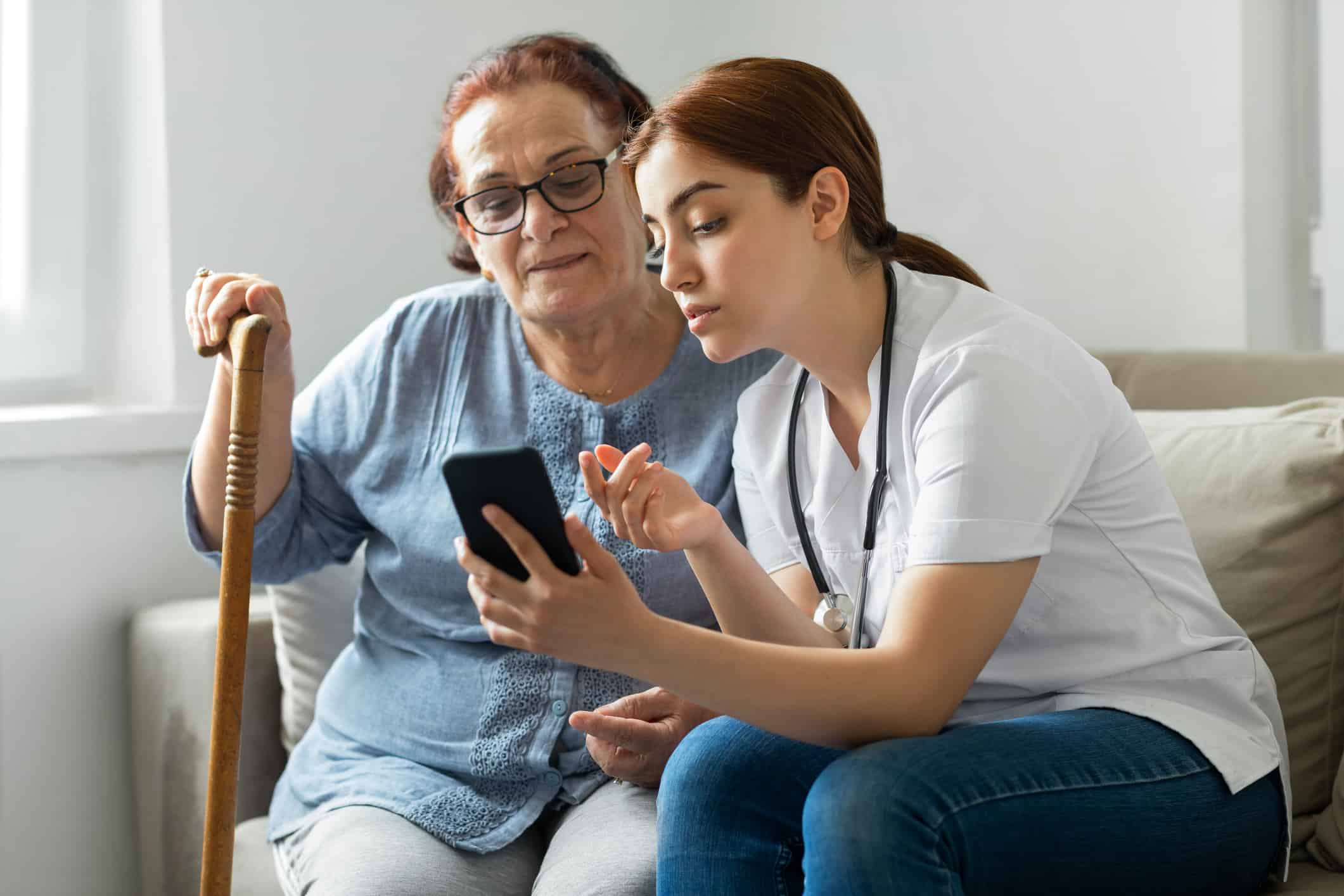 Senior woman with nurse at home with mobile phone